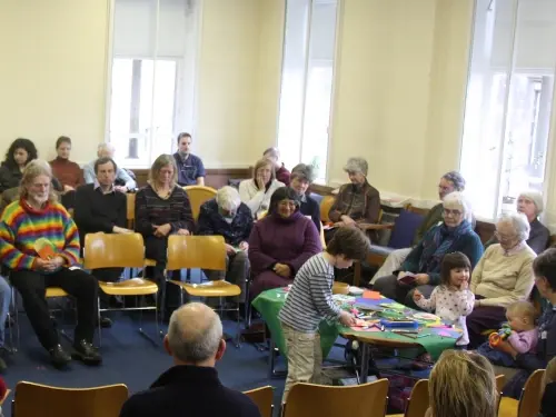 People of all ages sitting on chairs in a circle around a table in Meeting for Worship. 