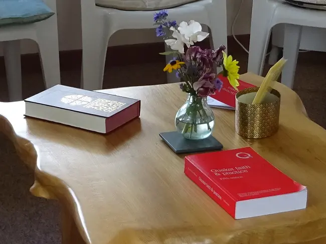 A table, on which is a copy of Quaker Faith and Practice, a copy of the Bible, and a vase of flowers. 