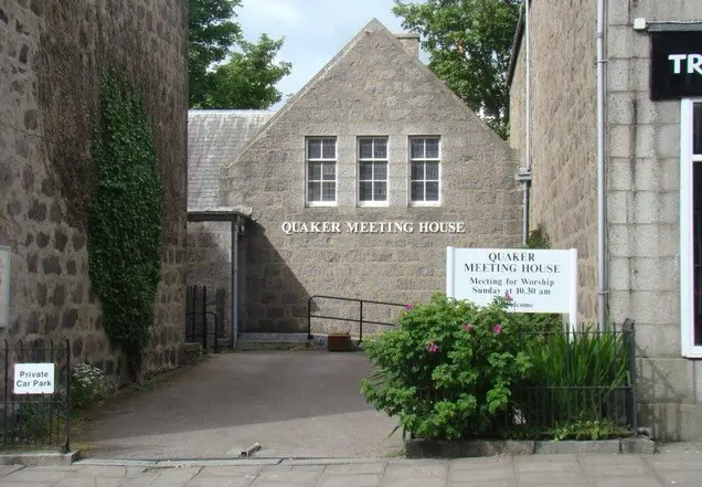 A Quaker Meeting House with a path leading up to it, with plants on either side of the path. 